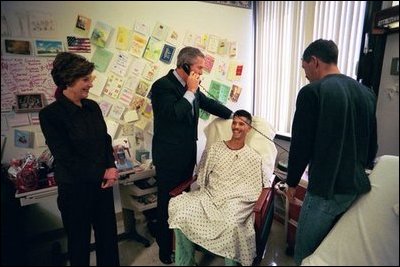 President George W. Bush speaks to a relative of U.S. Army Sergeant First Class Joseph Briscoe, of Liberty, Texas, after presenting Sgt. Briscoe The Purple Heart for injuries he sustained while serving in Iraq. President Bush visited troops at Walter Reed Army Medical Center in Washinton, D.C., Thursday, December 18, 2003. Laura Bush and Sgt. Briscoe’s brother, Ira, look on.