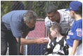 President George W. Bush greets Kevin Fulcher, Jr., 7 year old son of WHCA Tech. Sgt. Kevin Fulcher, Sr., during a White House Tee Ball (t-ball) game on the South Lawn between the Waynesboro, Virginia Little League Challenger Division Sand Gnats (Blue Team) vs. the East Brunswick, New Jersey Babe Ruth Buddy Ball League Sluggers (Red Team) September 22, 2002.