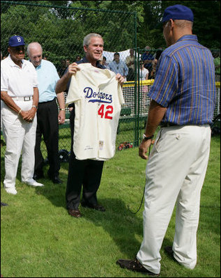 President George W. Bush holds up a commemorative baseball jersey with Jackie Robinson's number 42 presented to him by players from Robinson's playing era at the White House Tee Ball Game Sunday, July 15, 2007. Tee Ball players wore the number 42 to celebrate the legacy of Jackie Robinson.