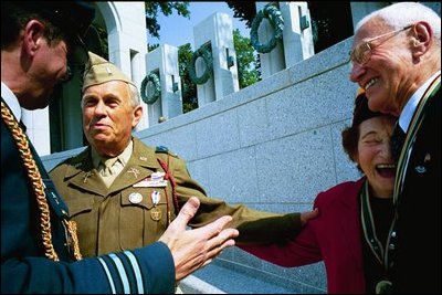 Battle of the Bulge veterans Dorothy S. Davis of Kensington, Md., right, embraces George Watson of Long Island, N.Y., right, as Earle R. Hart of Berwyn, Pa., speaks with Brigadier General Dany E. Van de Ven, Defense Cooperation Attaché of the Embassy of Belgium, far left. The group gathered to welcome visiting Belgian Foreign Minister Louis Michel, who came to lay a wreath at the memorial.